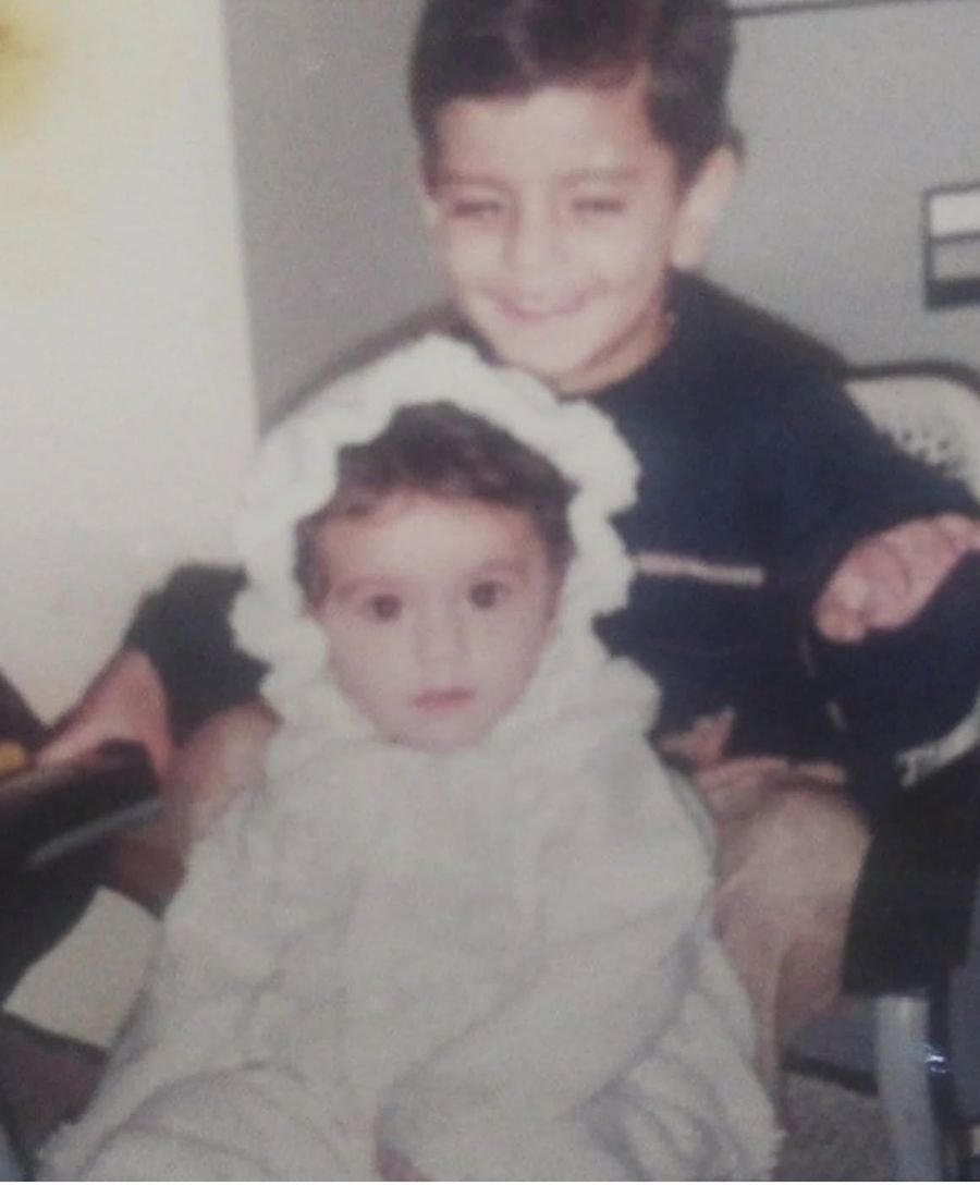 Nikunj as a young boy standing behind baby Divyanshi, who is dressed in a white bonnet and robe