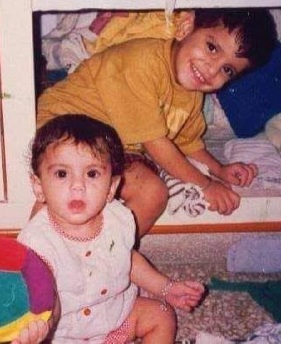 Nikunj in a yellow t-shirt crouched behind baby Divyanshi, who is sitting on the floor with a colourful ball
