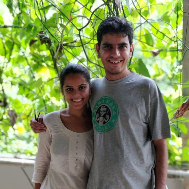 Divyanshi and Nikunj standing together outdoors under greenery, his arm around her shoulder