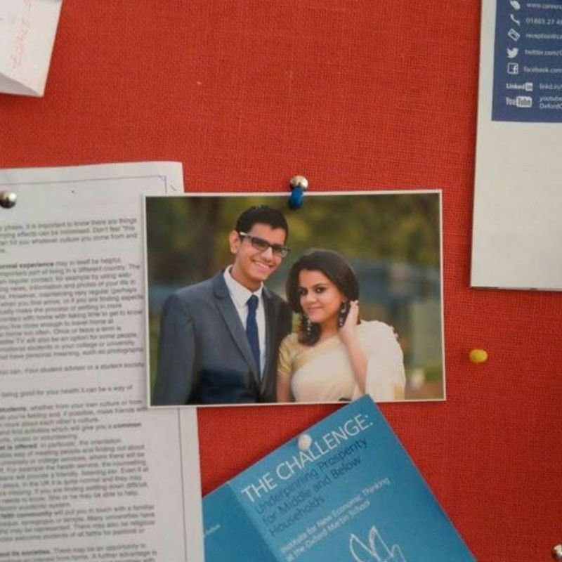 An old printed photo of the two of them pinned to a corkboard, surrounded by university flyers